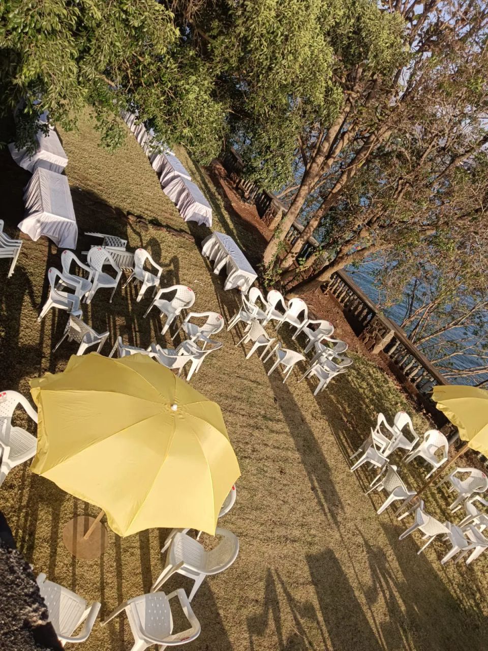 Outdoor lakeside lawn prepared with white banquet tables, chairs and yellow umbrellas for a corporate offsite