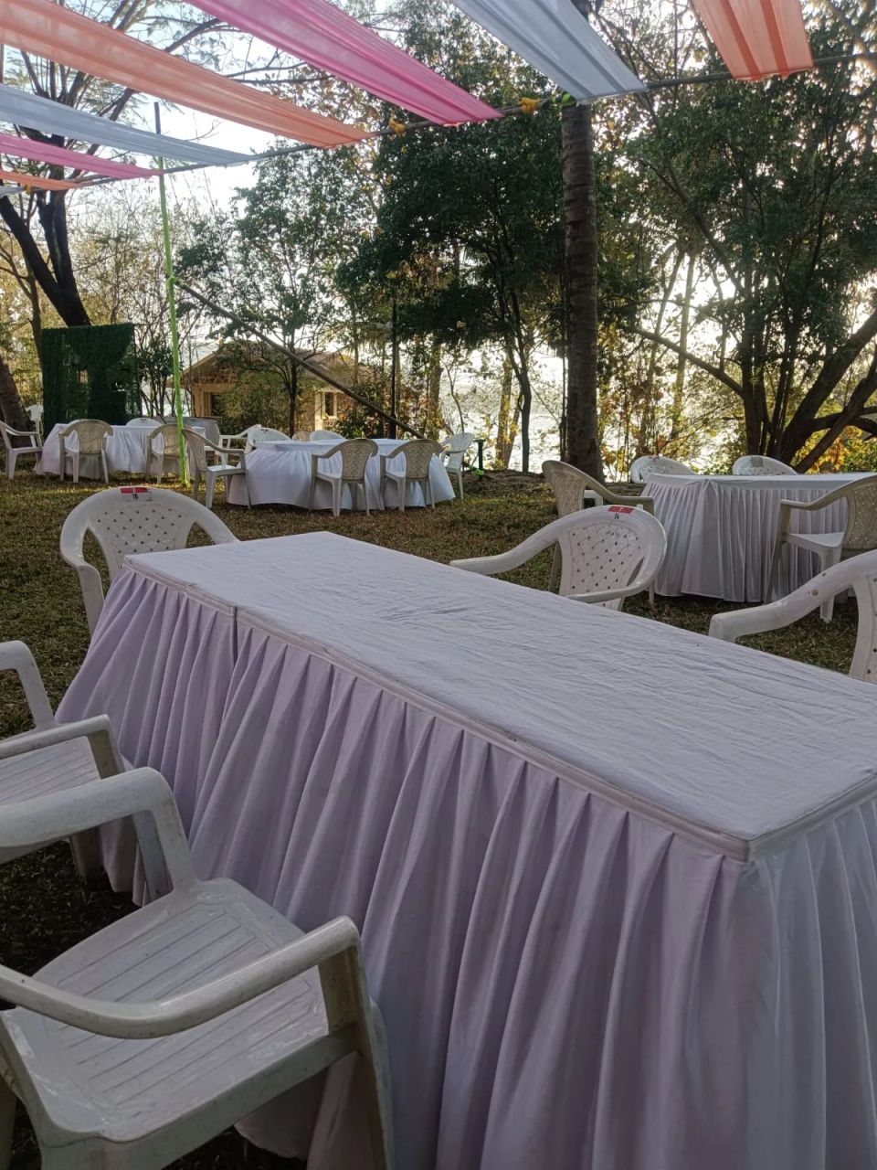 Outdoor banquet tables under pink and orange fabric canopy strips at a lakeside corporate gathering
