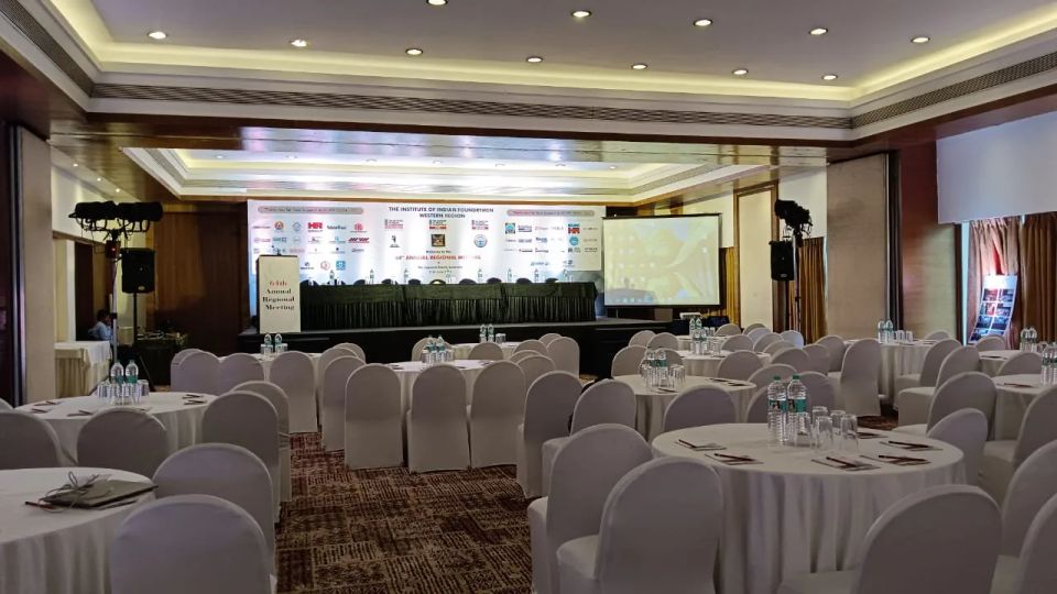 Banquet-style conference hall with round tables, white chair covers and a branded stage for an annual regional meeting